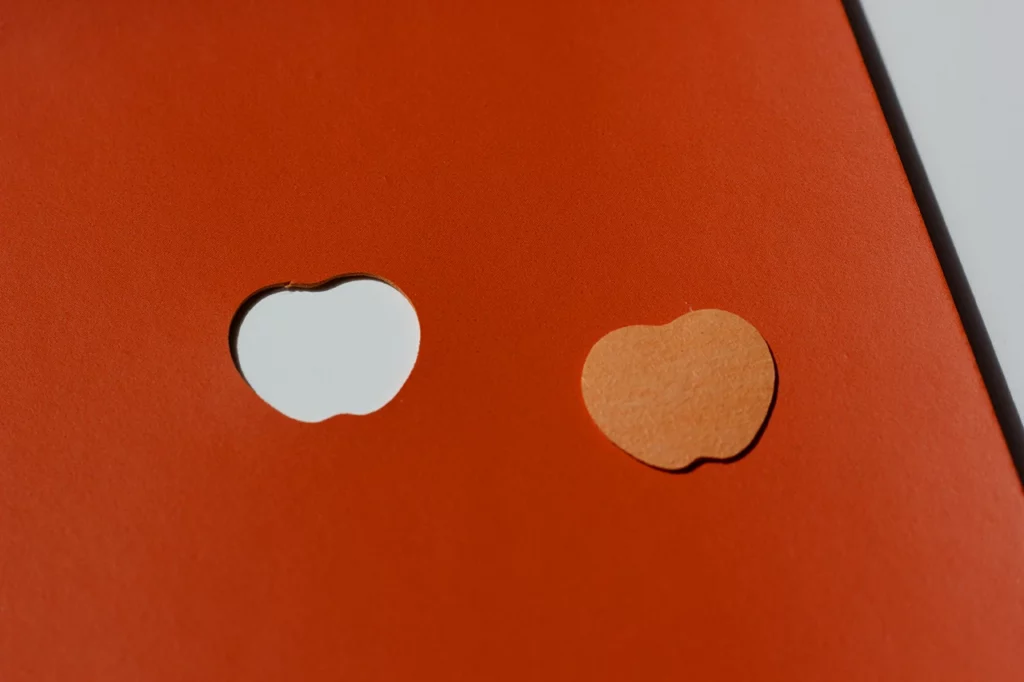Forme évidée et silhouette pleine d'une pomme, découpées dans du cuir de pomme orange (SIDRA), fourni par Schmedt. Forme évidée et silhouette pleine d'une pomme, découpées dans du cuir de pomme orange (SIDRA), fourni par Schmedt.