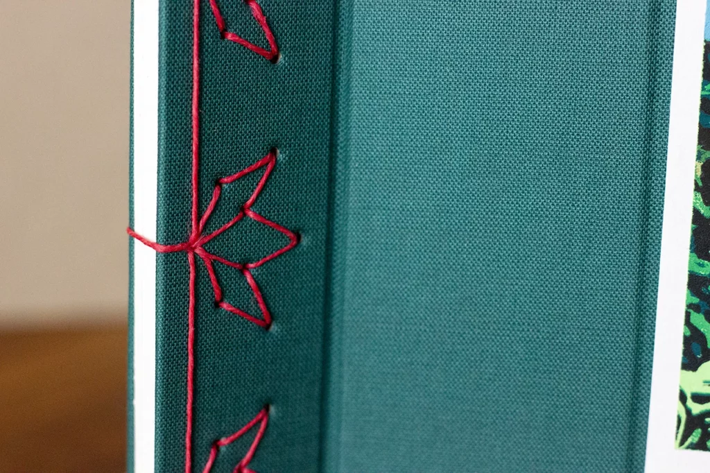 Zoom sur la reliure japonaise artisanale, avec un motif floral cousu au fil de lin ciré rose fuchsia.