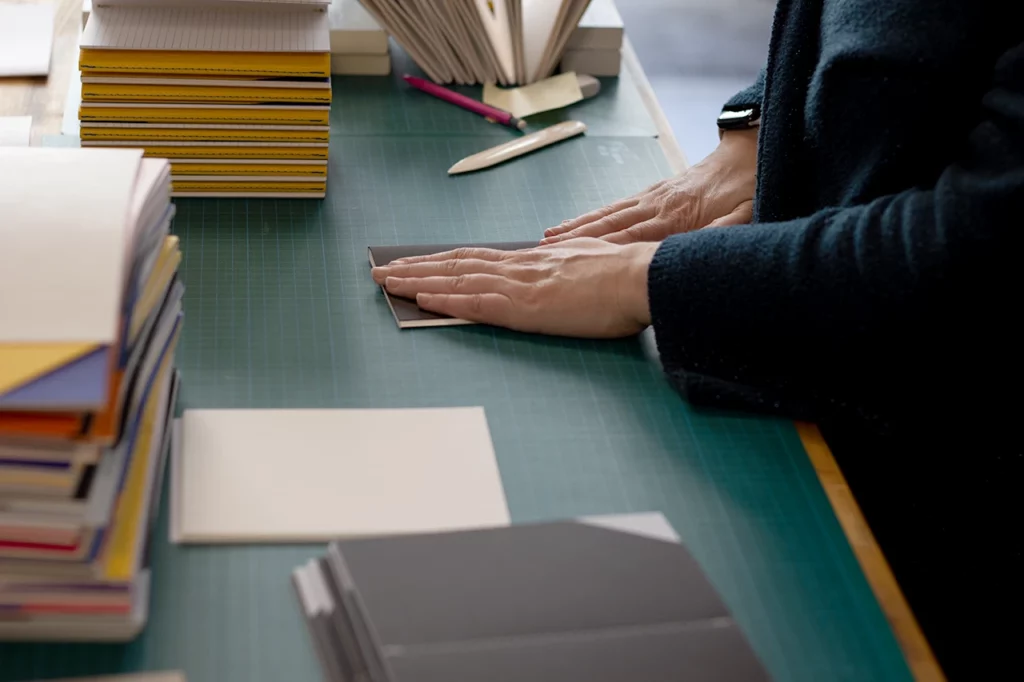 Façonnage des carnets bicolores de la nouvelle gamme de papeterie fine artisanale en édition limitée, après reliure Singer.