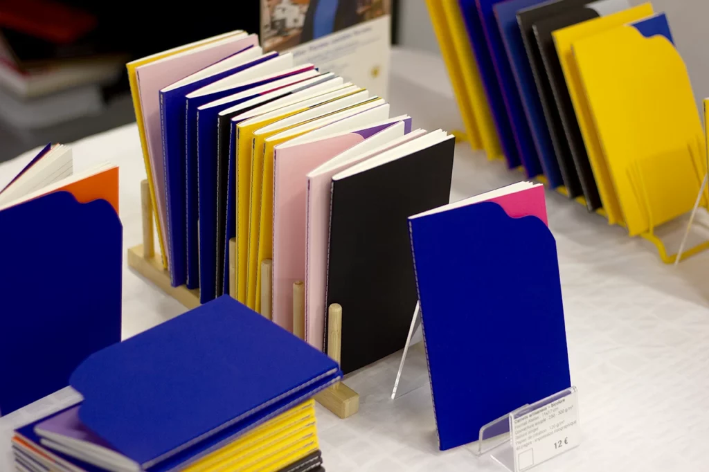 Vue des carnets bicolores format A6+, à formes organiques ou géométriques, présentés lors du salon de l’artisanat à La Teste-de-Buch.
