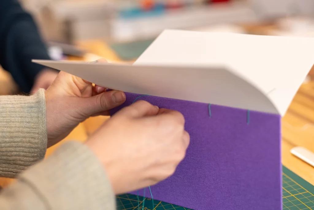 Passage du fil de lin ciré pour la réalisation d’un carnet en reliure copte, lors d’un atelier chez Forme contre forme à Bordeaux.