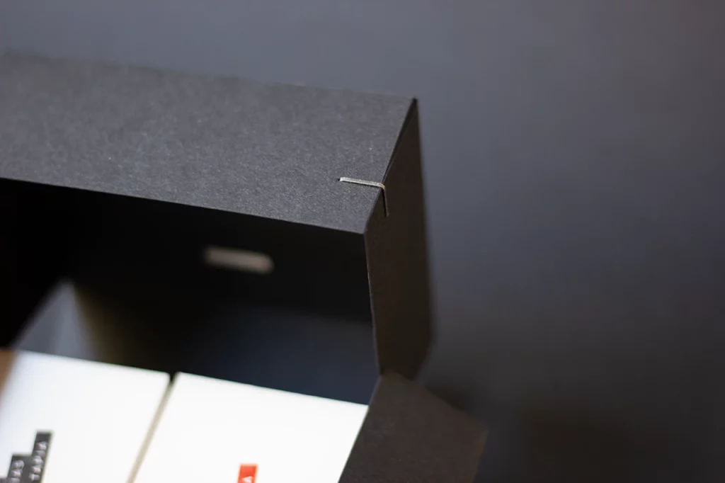 Zoom sur le haut de la boîte noire en papier Fedrigoni Materica Ardesia, mettant en valeur le système d’agrafes d’angle.