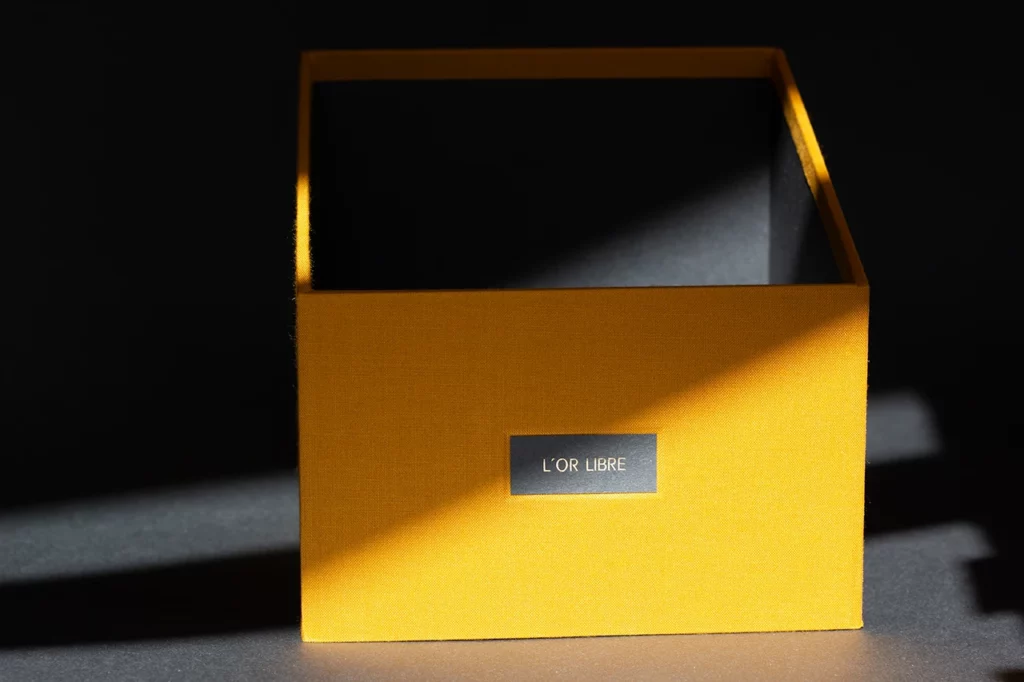 Zoom sur un angle d’une boîte de rangement rembordée en toile du Marais jaune moutarde, intérieur en papier Fedrigoni Materica Ardesia — Atelier Forme contre forme, Bordeaux.