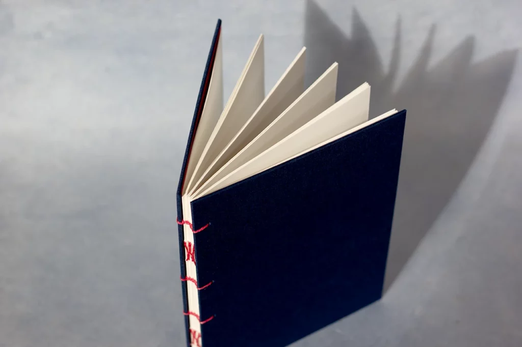 Carnet ouvert en reliure copte, couverture en toile du Marais bleu marine, couture au fil de lin rose fuchsia — vue de dessus — Atelier Forme contre forme, Bordeaux.