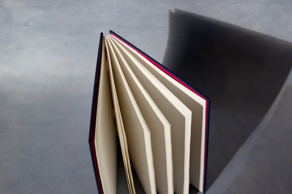 Carnet ouvert en reliure copte, couverture en toile du Marais bleu marine, page de garde rose — vue de dessus — Atelier Forme contre forme, Bordeaux.