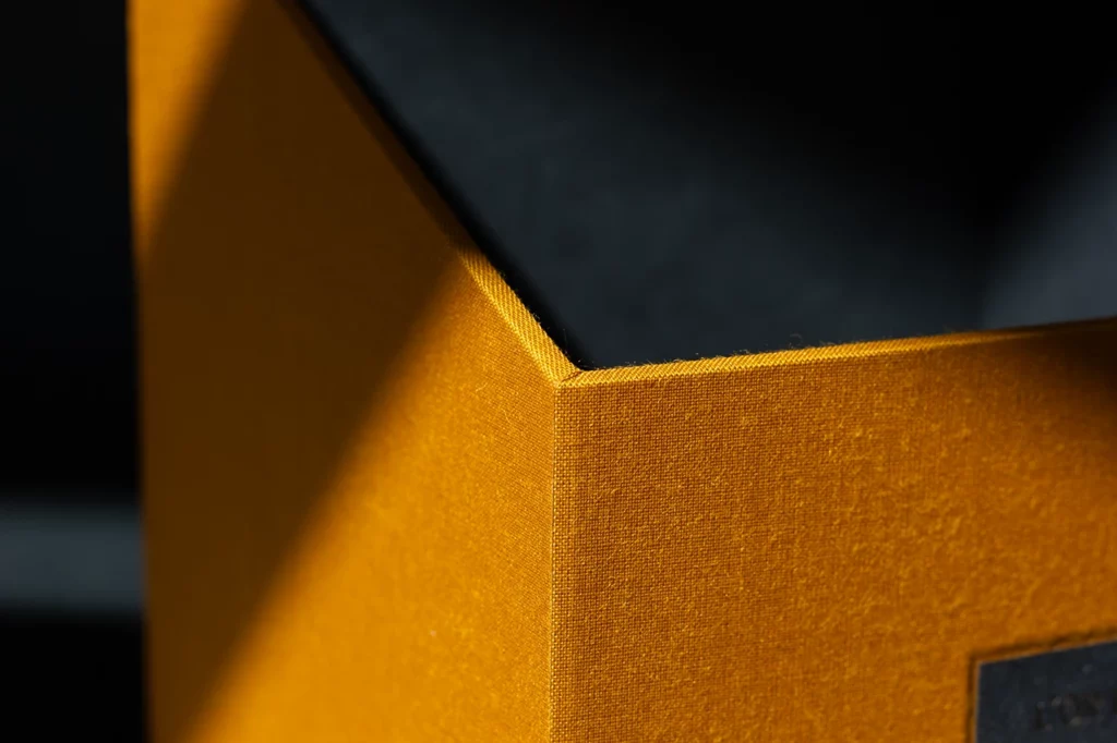 Zoom sur la finition d’un angle de boîte de rangement rembordée en toile du Marais jaune moutarde — Atelier Forme contre forme, Bordeaux.