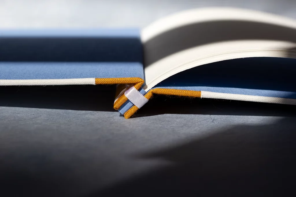 Zoom sur la structure d’un carnet en reliure japonaise ouvert à plat, gardes en toile du Marais bleue — Atelier Forme contre forme, Bordeaux.