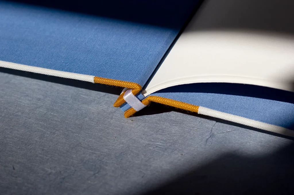 Zoom sur la structure d’un carnet en reliure japonaise ouvert à plat, gardes en toile du Marais bleue — Atelier Forme contre forme, Bordeaux, bis.