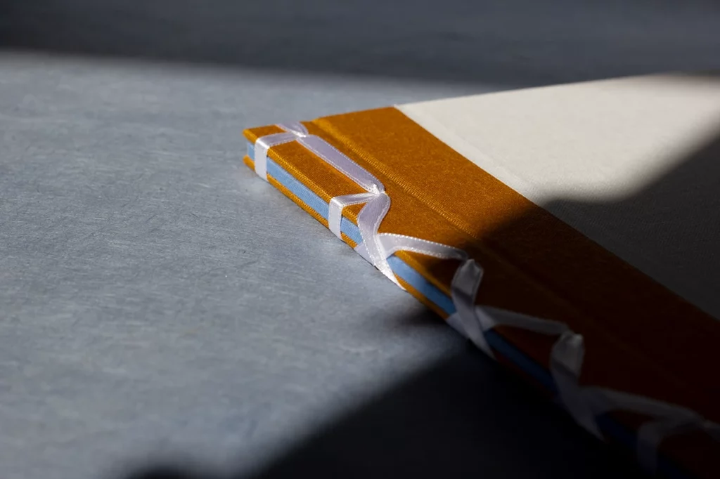Zoom sur le haut du carnet en reliure japonaise avec ruban satiné blanc, dos en toile bleue apparent — Atelier Forme contre forme, Bordeaux.