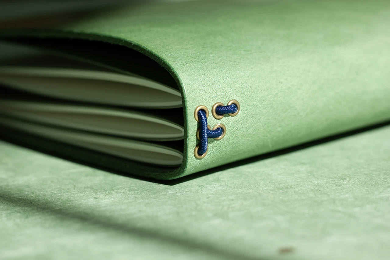 Zoom sur le passage des élastiques dans des œillets en bronze formant un “F”, signature Forme contre forme.