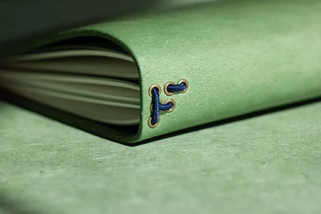 Zoom sur le passage des élastiques dans des œillets en bronze formant un “F”, signature Forme contre forme — vue bis.