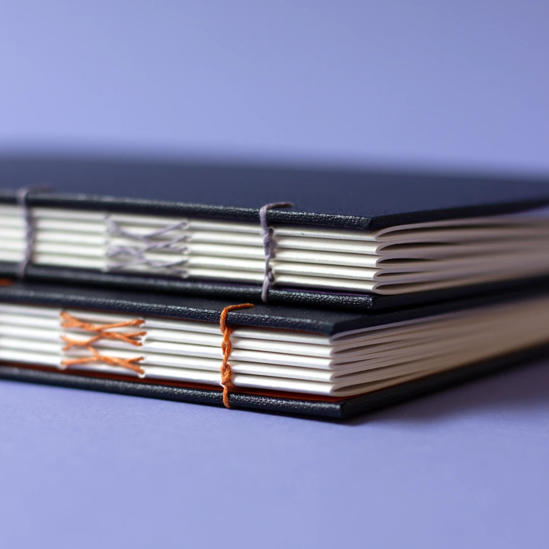 Zoom sur les chaînettes de la reliure copte de deux carnets sur mesure, couverture similicuir noir et papier Fedrigoni — à plat — Atelier Forme contre forme, Bordeaux.