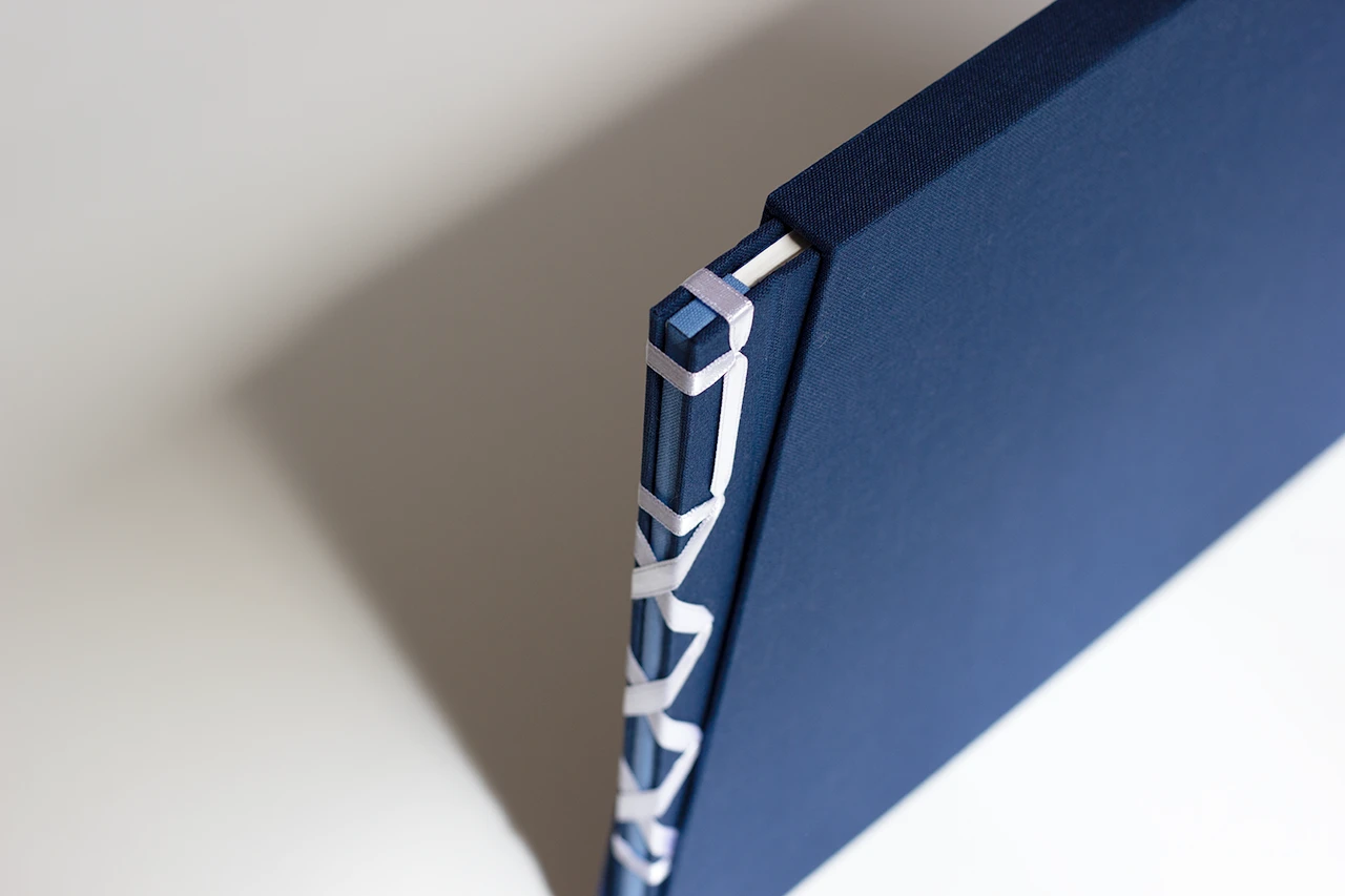 Livre d’or de mariage en reliure japonaise, ruban satiné blanc, toiles bleu marine et bleu clair, inséré dans son fourreau sur mesure — Atelier Forme contre forme, Bordeaux.