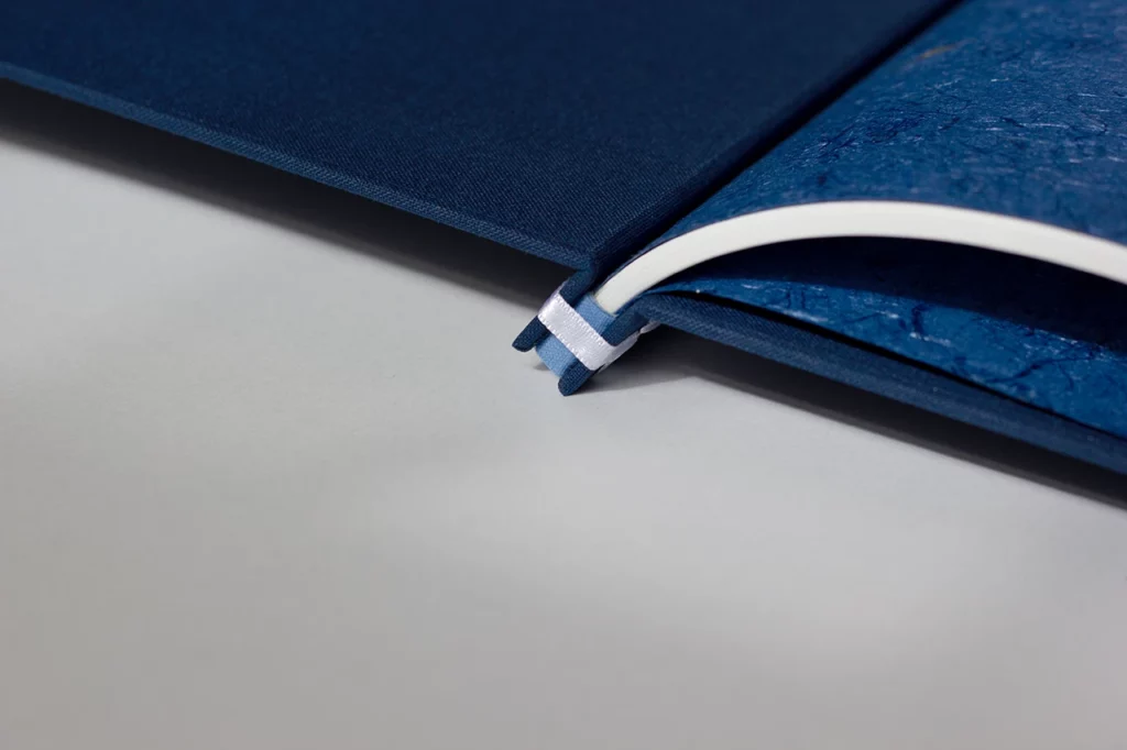 Zoom sur la structure d’un livre d’or en reliure japonaise ouvert à plat, pages de garde en papier népalais bleu — Atelier Forme contre forme, Bordeaux.