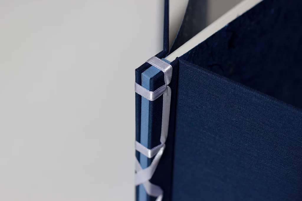 Zoom sur le haut de la structure du livre d’or en reliure japonaise, ruban satiné blanc et toiles bleu marine et bleu clair — Atelier Forme contre forme, Bordeaux.