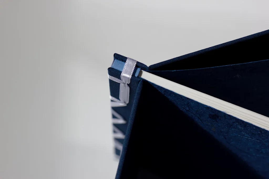 Zoom sur le haut du livre d’or en reliure japonaise, ruban satiné blanc et toiles bleu marine et bleu clair — Atelier Forme contre forme, Bordeaux.