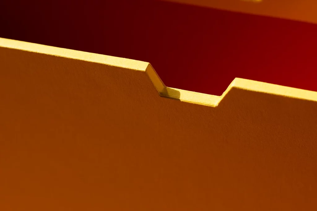 Zoom sur une encoche de préhension (« coup de pouce ») en perspective sur un fourreau rigide sur mesure, papier Fedrigoni Materica Terra Gialla et Terra Rossa — Atelier Forme contre forme, Bordeaux.
