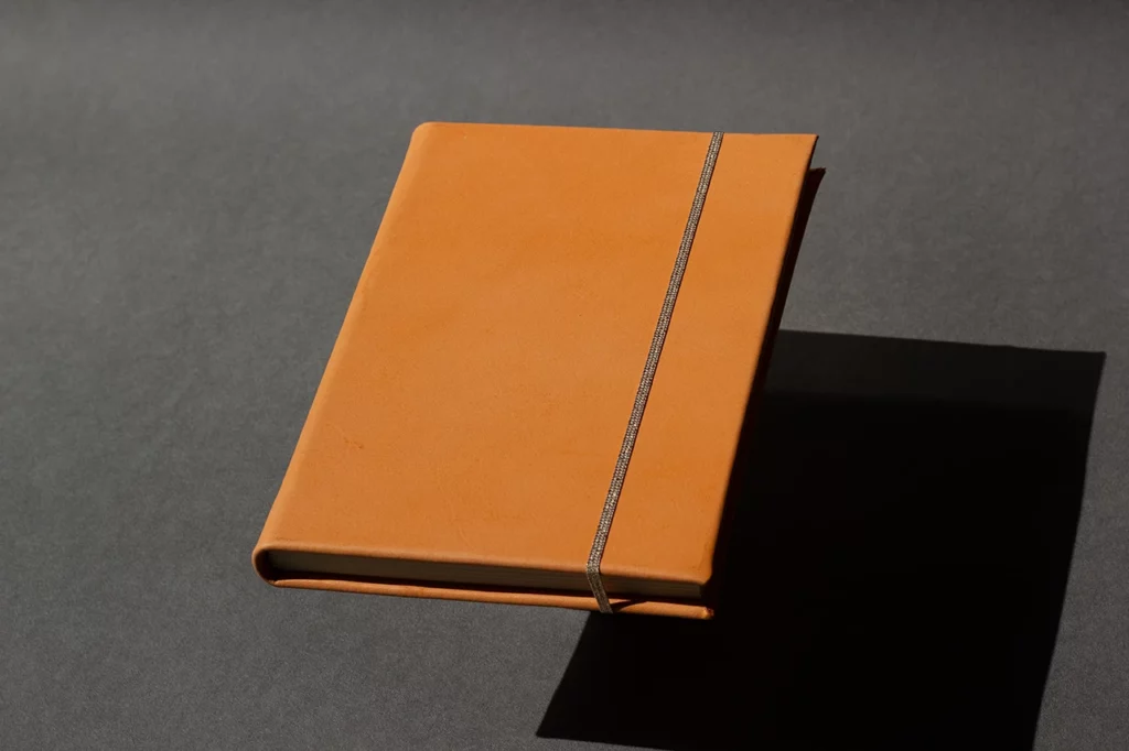 Carnet en cuir orange réalisé lors d’ateliers sur mesure, avec couverture rigide en cuir sellier végétal — Atelier Forme contre forme, Bordeaux.