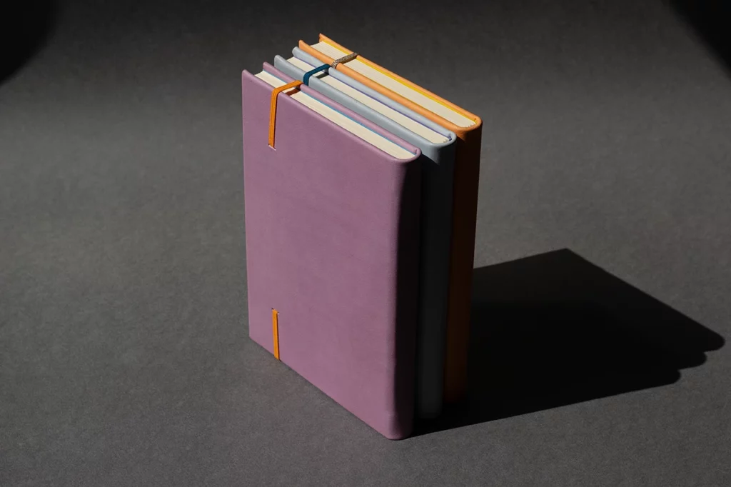 Carnets en cuir artisanaux réalisés en atelier sur mesure, en cuir sellier végétal pastel orange, bleu et mauve avec fermeture élastique — Atelier Forme contre forme, Bordeaux.