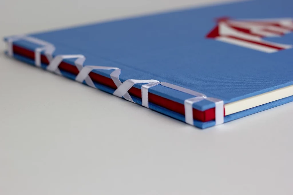 Dos en papier népalais main rouge d’un livre sur mesure en reliure japonaise à ruban blanc, avec couverture en toile du Marais — Atelier Forme contre forme, Bordeaux.