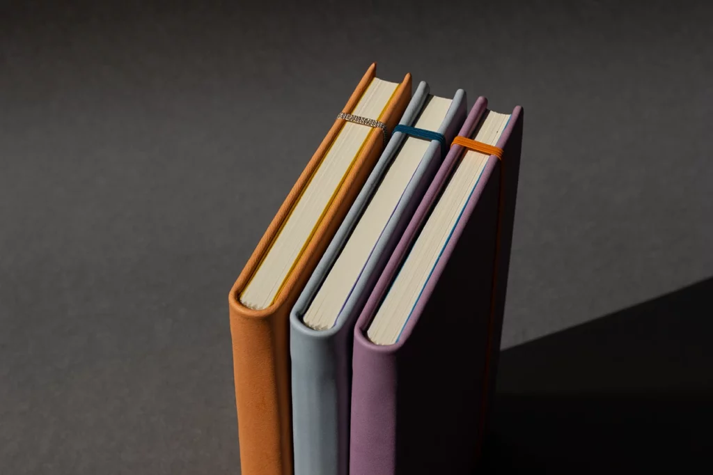 Trio de carnets en cuir artisanaux réalisés lors d’un atelier sur mesure, en cuir sellier végétal pastel orange, bleu et mauve — Atelier Forme contre forme, Bordeaux.